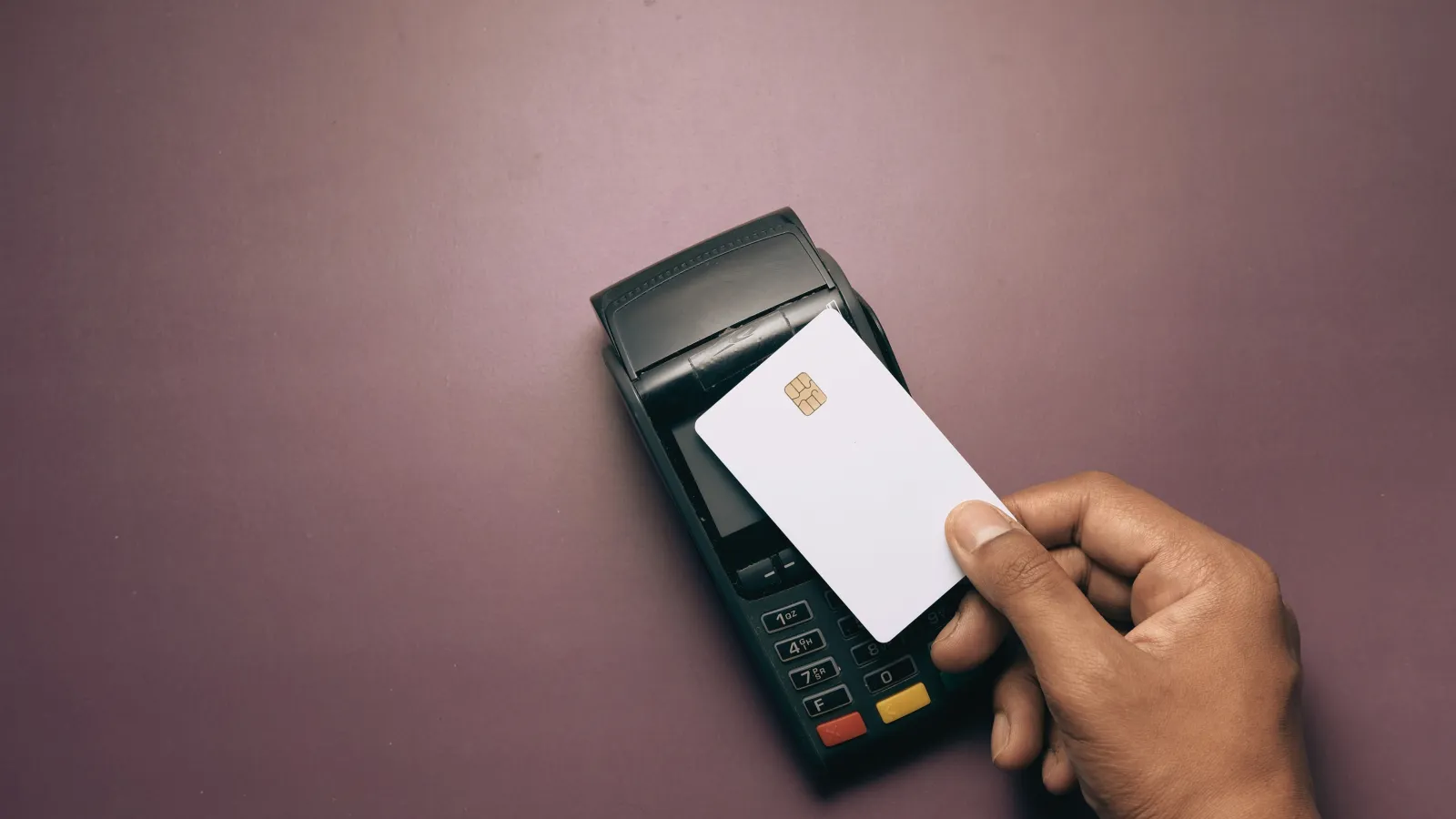 A hand tapping a white chip card on a black payment terminal